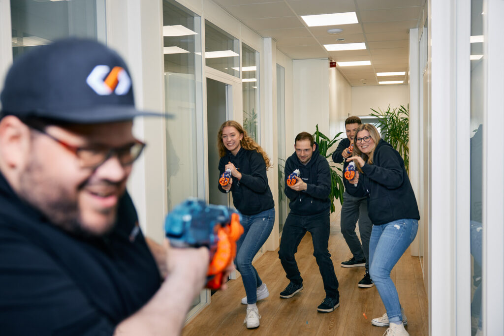 Kolleg:innen posieren mit Werkzeugen und Humor im Flur.